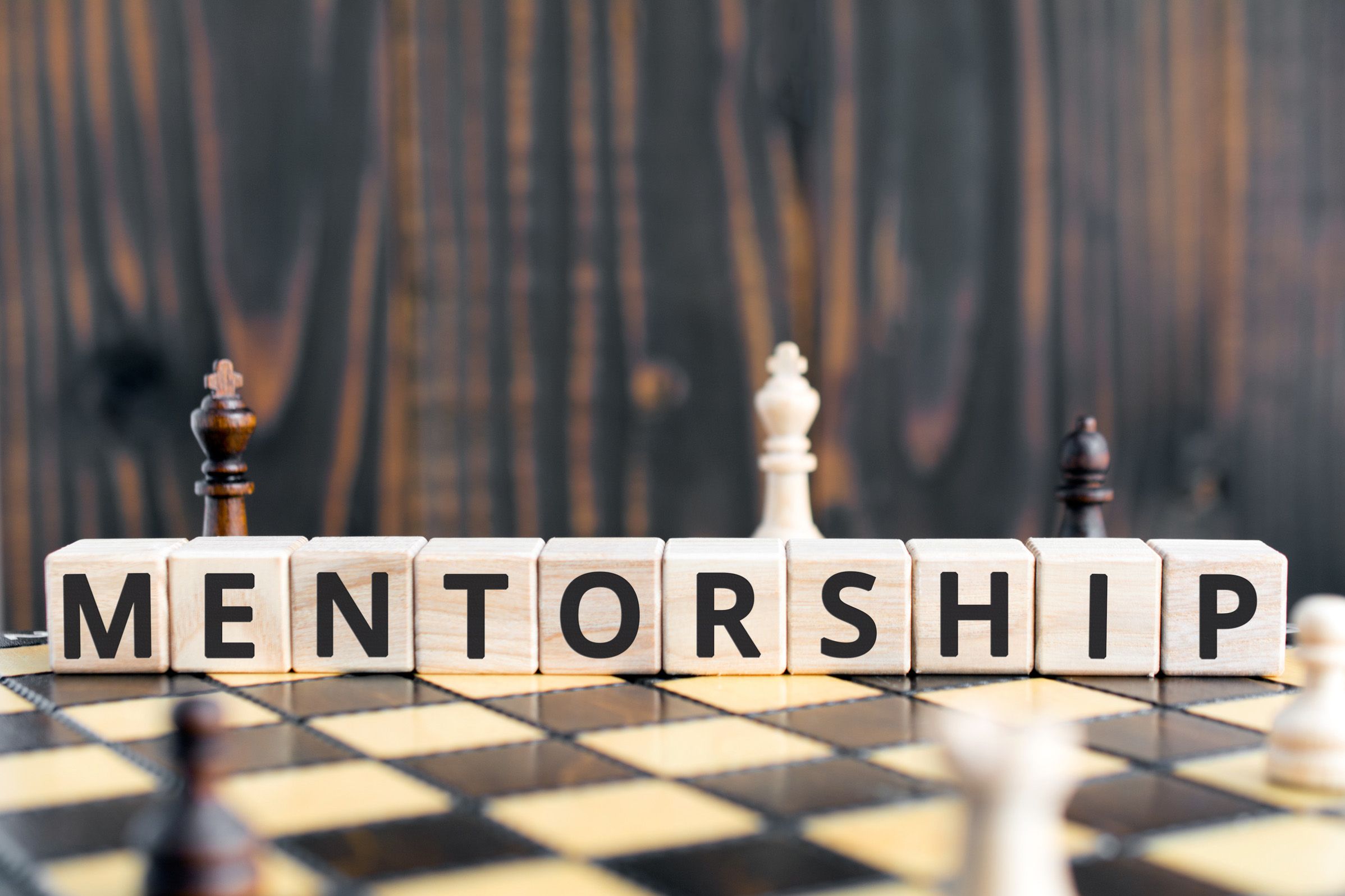 Wooden blocks on a chess board spelling out the word Mentorship.